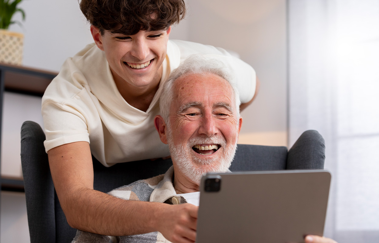 Chico joven y hombre mayor sonrientes mientras miran una tablet